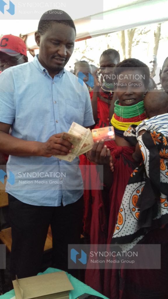 Devolution CS Mwangi Kiunjuri hands Emmy Ekiru cash and a Drought Emergency Scale-up card