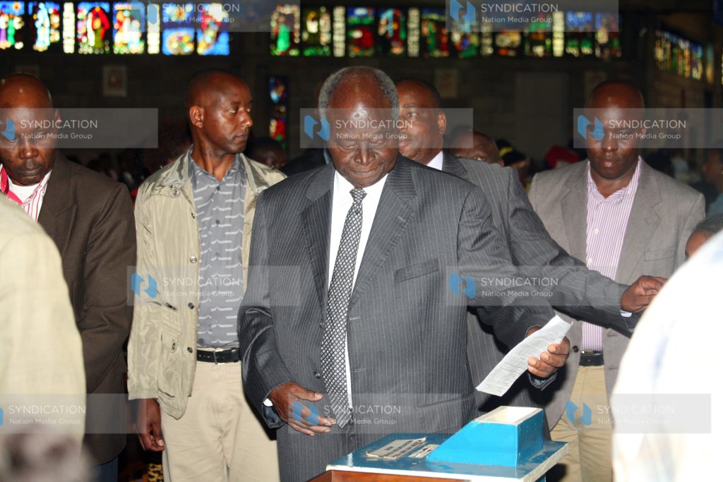 Former President Mwai Kibaki picking a booklet containing the program