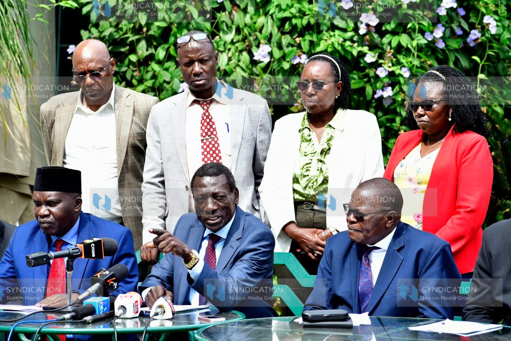 Collins Oyuu (seated center) gestures during a joint media briefing
