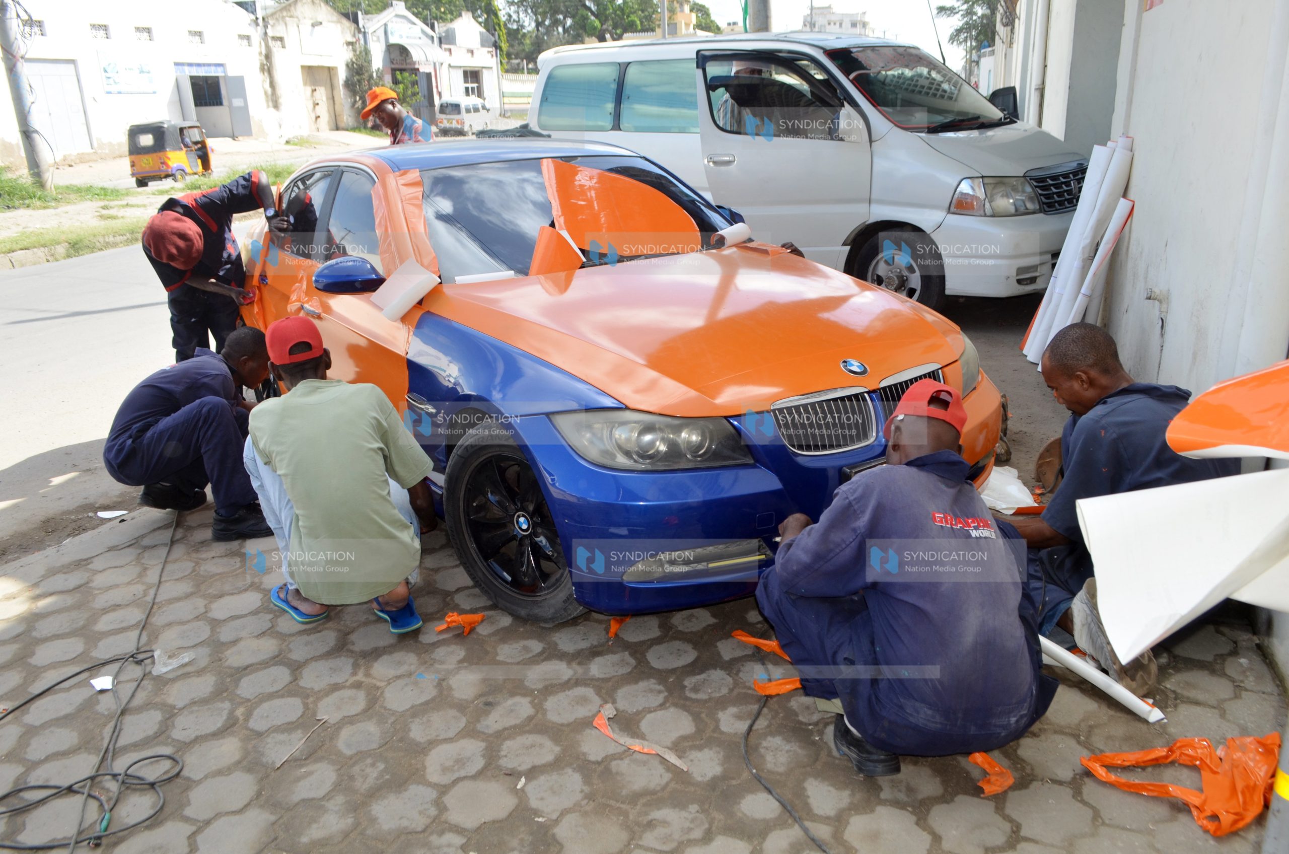 Workers proceed with branding a saloon car with ODM Party colours