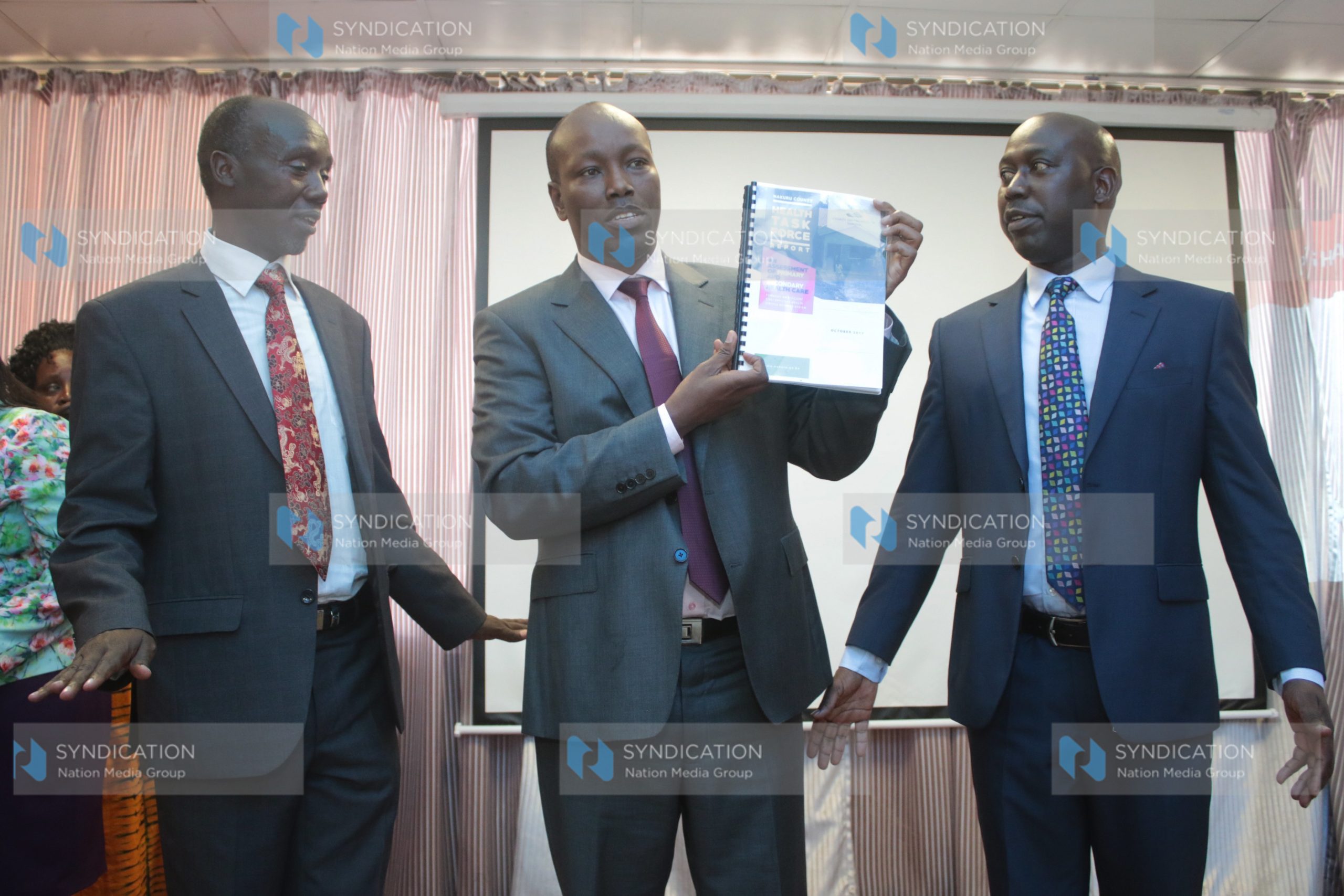 James Tuitoek (left) hands over its findings to Nakuru County Governor Lee Kinyanjui (centre)