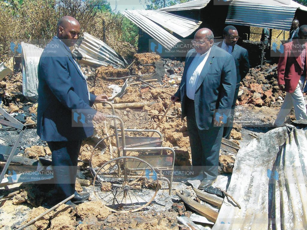 Former Tanzania president Benjamin Mukapa looks at a wheelchair of one of the victims of Kenya Assemblies of God Church in Kiambaa