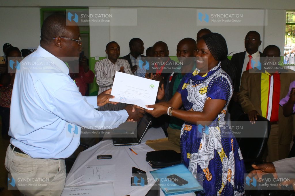 Kisii County Electoral and Boundaries Commission Returning Officer Dr. Sydney Namlanga (left) presents a nomination certificate